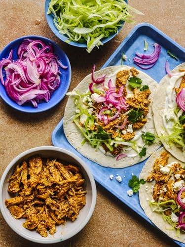 Tacos topped with shredded chicken, red onions, and greens on a blue serving tray.