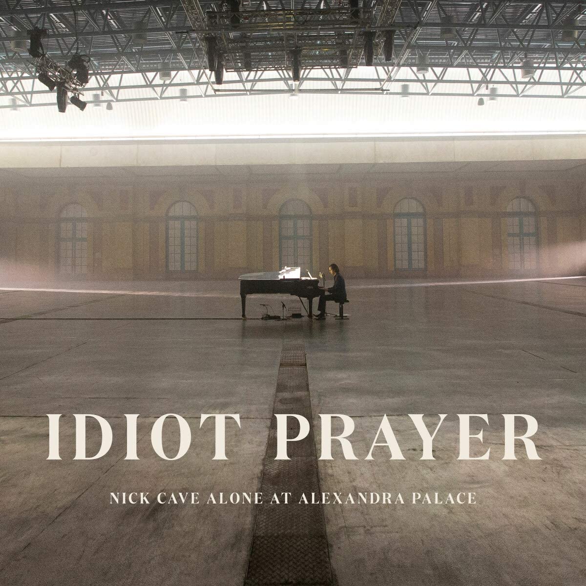 "CD cover featuring Nick Cave alone at a grand piano in a large, dimly lit hall."