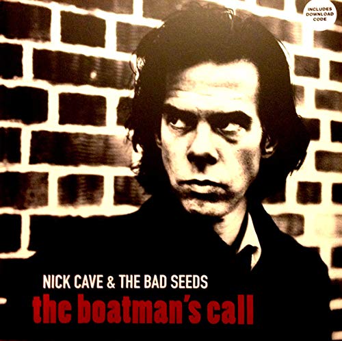 Black and white portrait of Nick Cave in front of a brick wall.