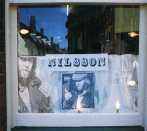 Harry Nilsson album cover displayed in a shop window with lit candles.