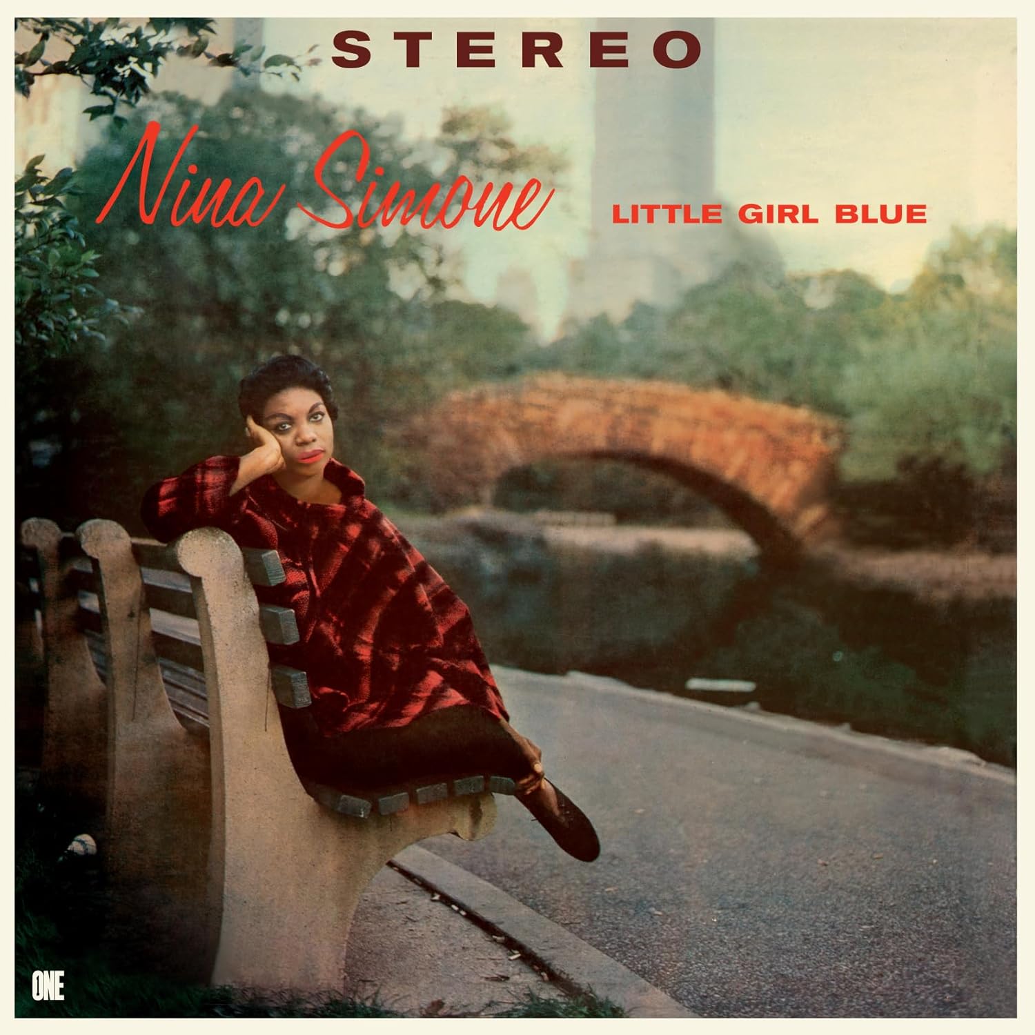 Nina Simone sits on a park bench with a stone bridge in the background.