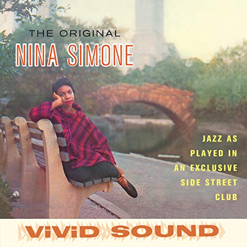 Nina Simone sitting on a park bench with a stone bridge in the background.