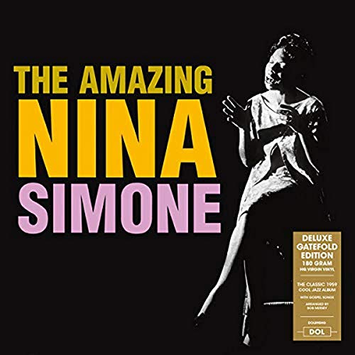 Black and white photo of Nina Simone sitting on a stool against black background.