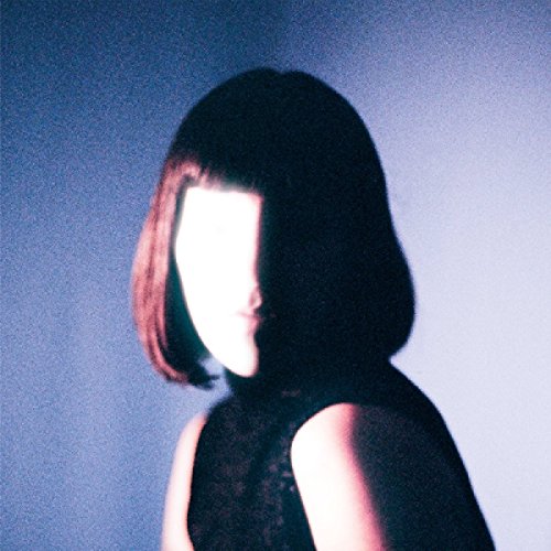 Woman with chin-length dark hair and black sleeveless top, face obscured by shadow and light.