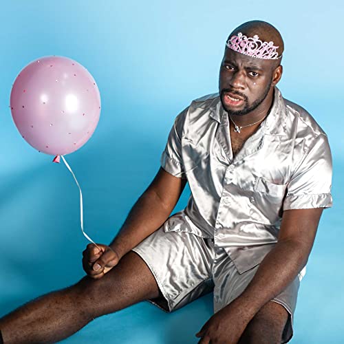 Black man in silver pajamas holding a pink balloon, wearing a tiara.