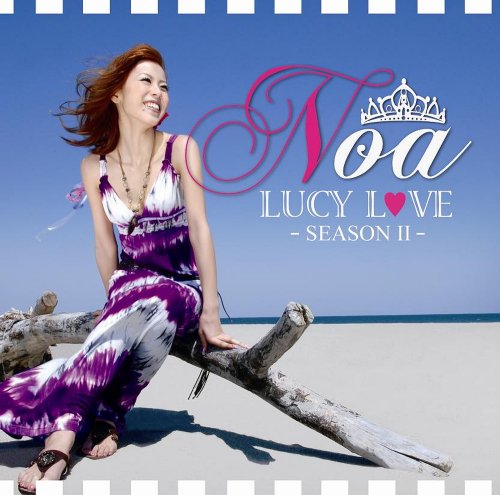 A woman in a purple tie-dye dress sits on driftwood on a sandy beach.