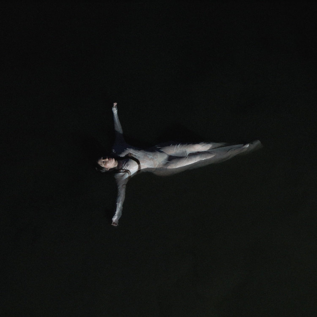 Noah Cyrus lying prone in darkness, arm raised, album cover art.