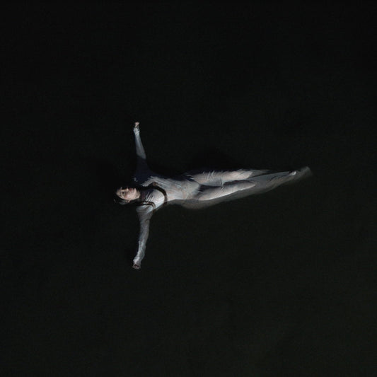 Noah Cyrus lying prone in darkness, arm raised, album cover art.