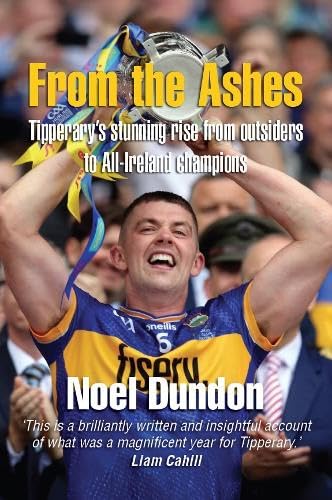 A Tipperary hurling player wearing a blue and gold jersey lifts a trophy overhead.
