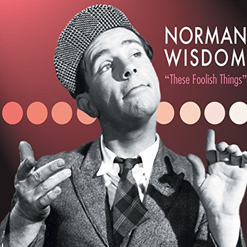 Norman Wisdom in a checkered cap, looking upwards with hands raised.