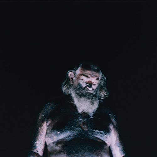 Close-up of a bearded man with a weathered face in low light.