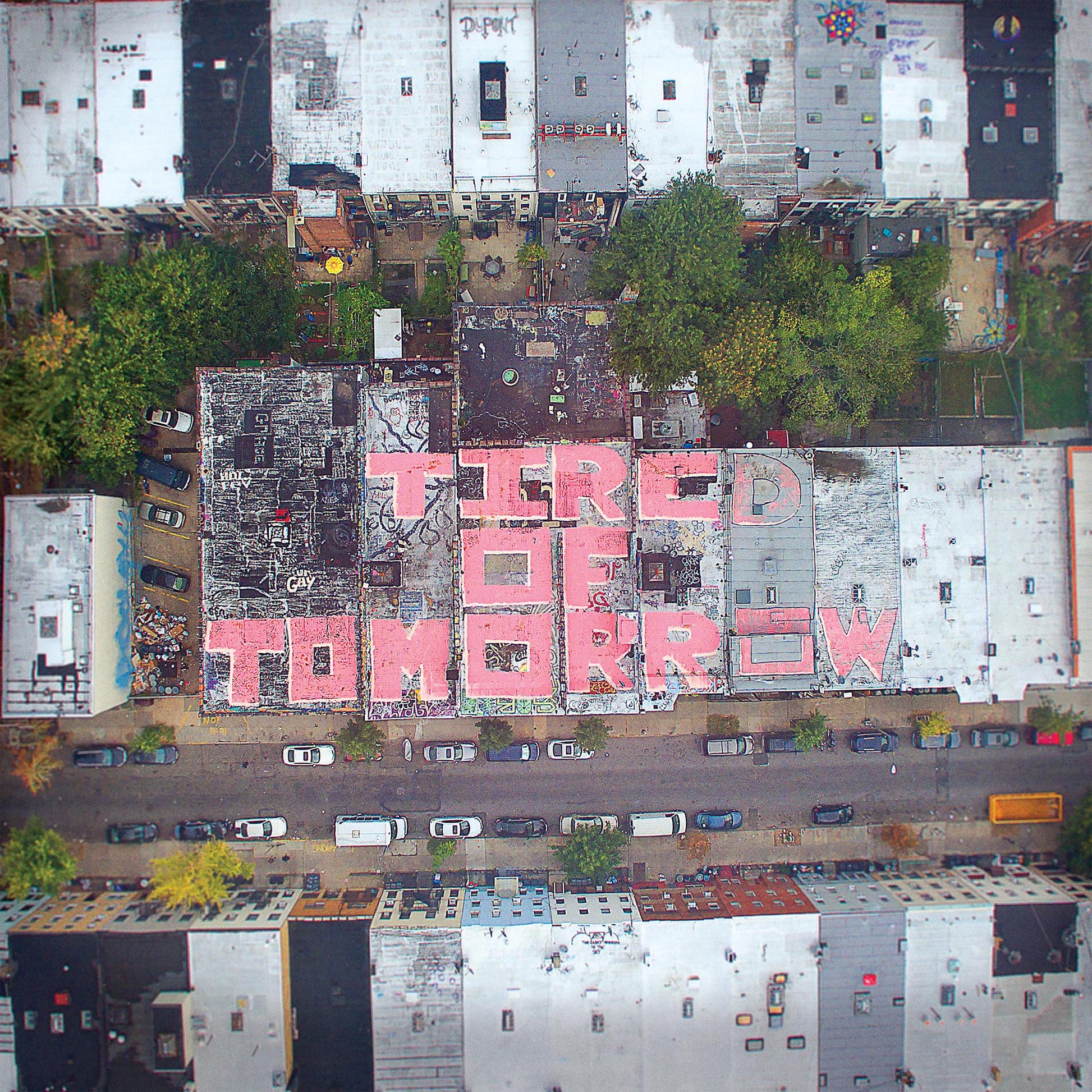 Aerial view of rooftops with pink graffiti reading "TIRED OF TOMORROW".