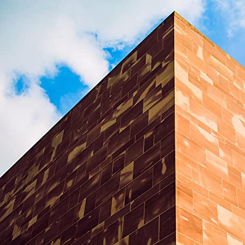 Close-up of a brown, textured building corner against a blue sky.