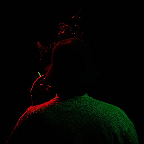 Dark silhouette of a person smoking, lit by red and green light.
