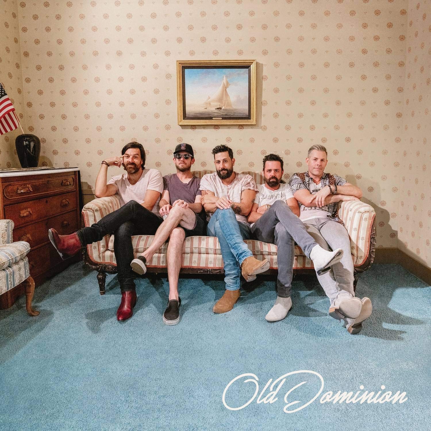 "Album cover with five men sitting on a couch in a retro-styled room."