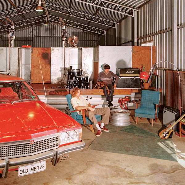 Two men and a dog sit amongst musical equipment in a garage.