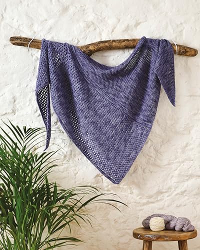 A purple crocheted triangular shawl hangs on a wooden branch against a white wall.