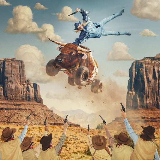 Man in blue jumpsuit rides bucking bull as cowboys shoot guns below.