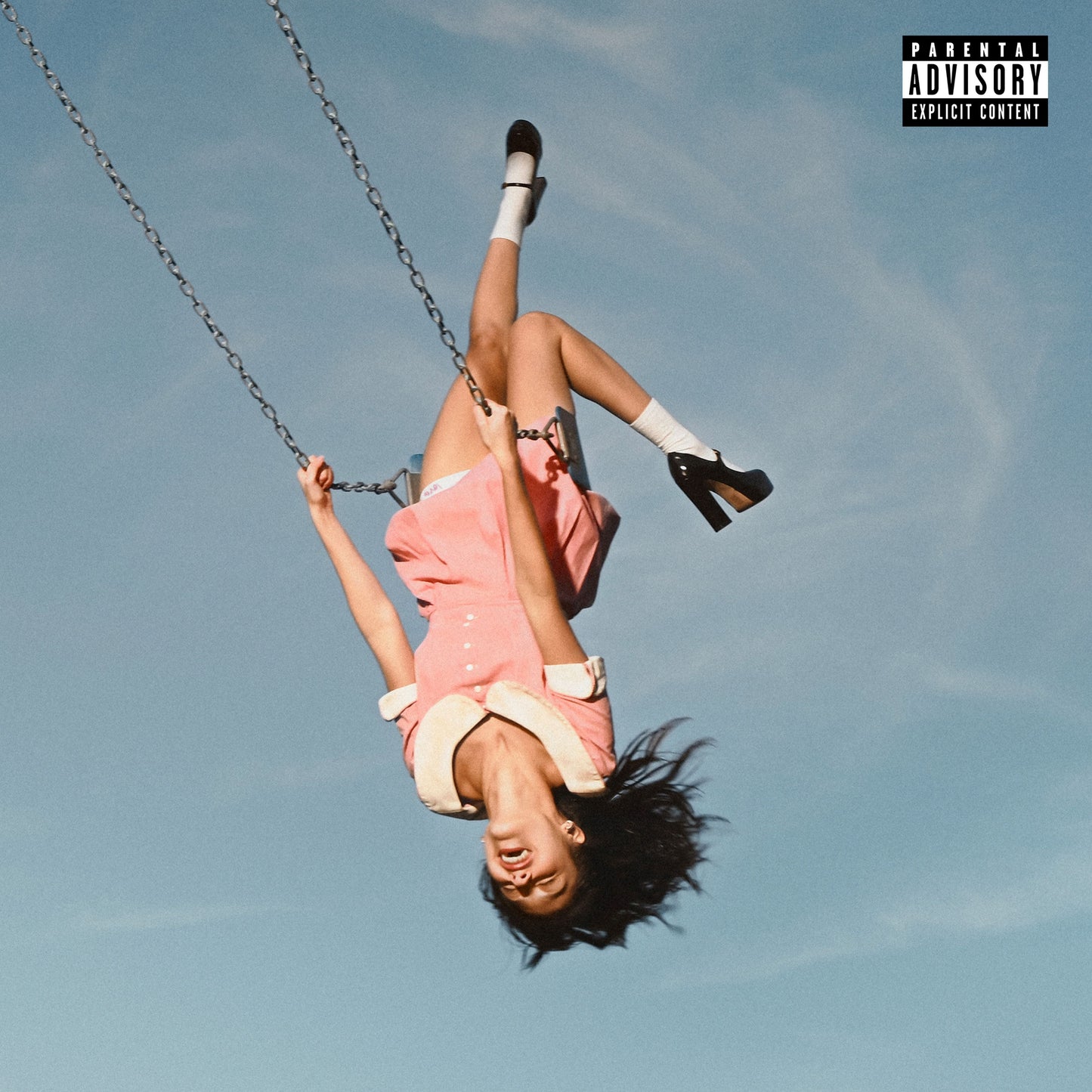 A girl in a pink dress hanging upside down on a swing against blue sky.