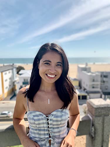 Woman with long dark hair smiling, beach and buildings in background.