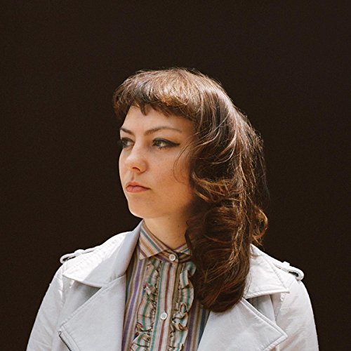 Portrait of Angel Olsen, a woman with brown hair, wearing a white jacket.