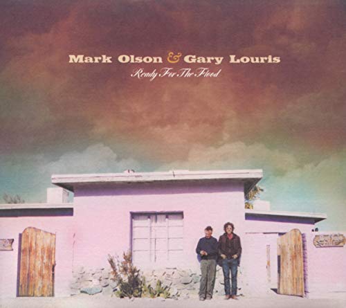 Two men stand in front of a pink building under a dramatic cloudy sky.