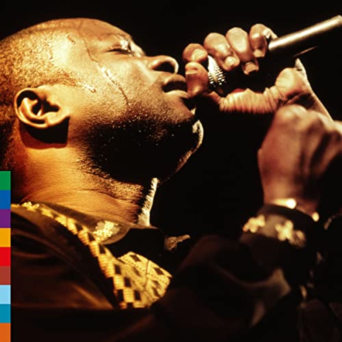 Omar Pene singing into a microphone, low-angle, warm lighting.