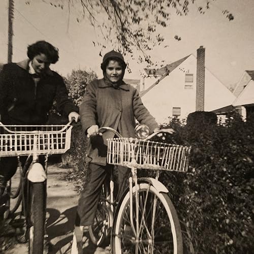 Two women with bicycles pose outdoors in a vintage, sepia-toned photograph.