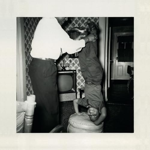Black and white photo of a man playfully holding a child upside down.