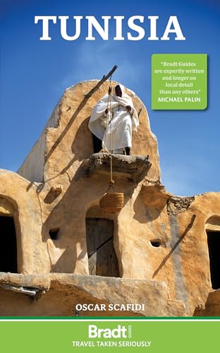 A person in traditional clothing stands on a mud-brick building lowering a woven basket.