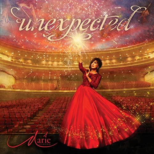 Marie Osmond in a red gown on a stage with fireworks and an audience.