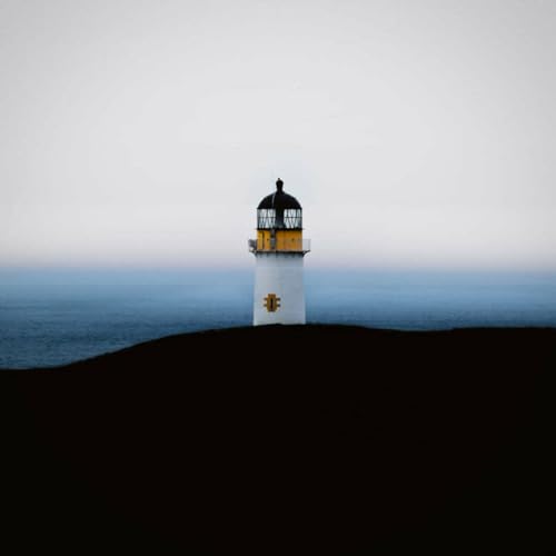 White lighthouse with black lantern room on a dark coastline.