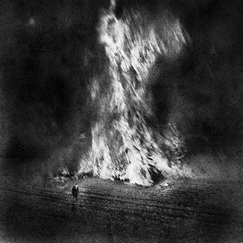 Black and white image of a person standing before a large fire or explosion.
