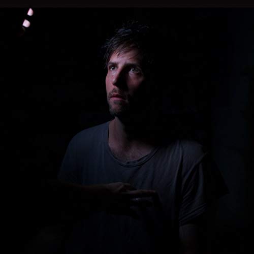 Man in a dark blue shirt is illuminated in a dark environment.