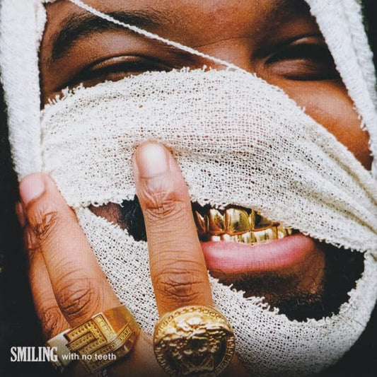 Close-up of a person with bandaged eyes and gold teeth smiling.