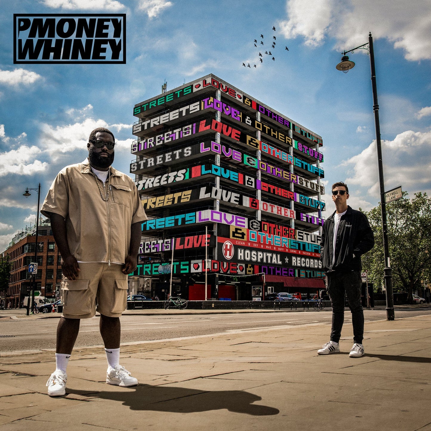 P Money and Whiney stand before a multi-story building featuring colorful text on its facade.