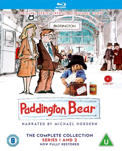 Paddington Bear standing with a suitcase next to a man and woman at Paddington.