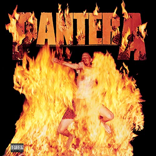 A man in plaid shorts stands amidst large flames below the fiery Pantera logo.