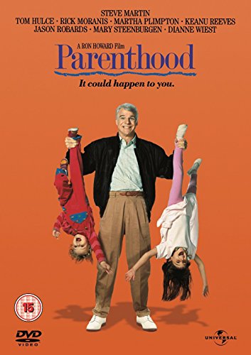 Steve Martin stands holding two children upside down against an orange background.
