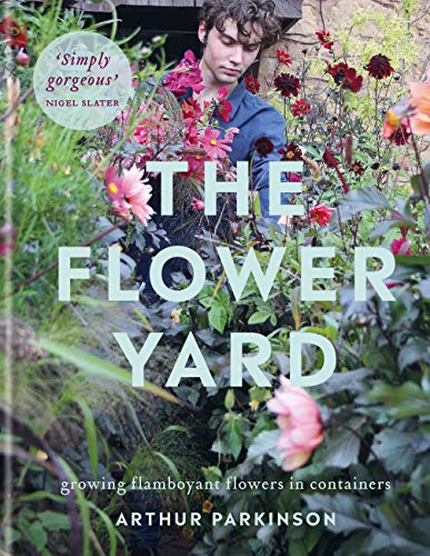A man tending to a lush garden of pink and red flowers.