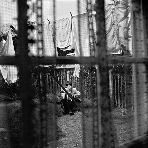 Black and white photo of Paul McCartney with a guitar in a backyard.