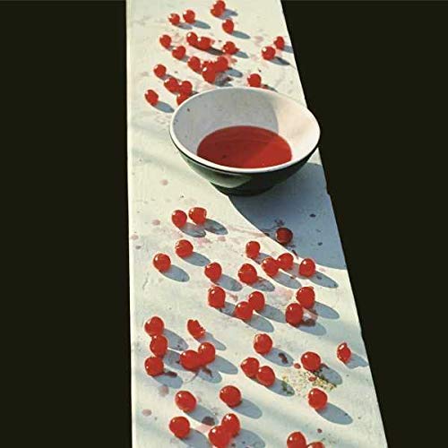 A bowl of red liquid surrounded by scattered cherries on a white surface.