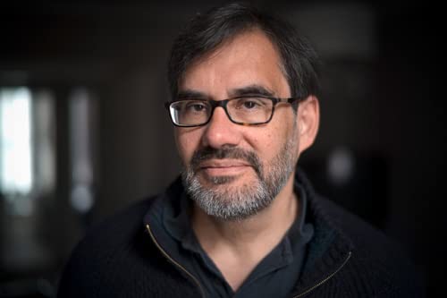 A portrait of a middle-aged man with a beard and glasses wearing a sweater.
