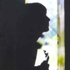 Silhouette of a person holding a guitar against a bright doorway.