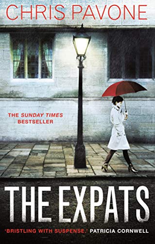 A woman with a red umbrella walks past a streetlamp in front of stone buildings.