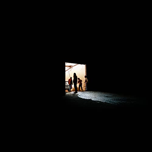 Silhouetted figures stand in a brightly lit doorway against darkness.