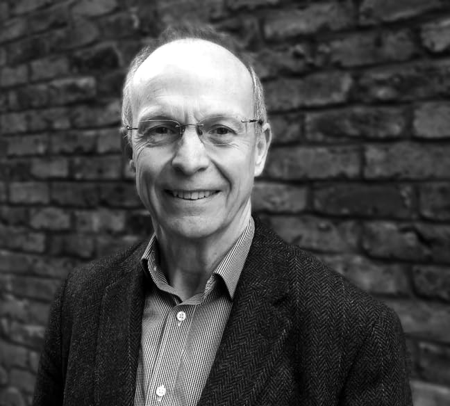 Black and white portrait of a smiling middle-aged man wearing glasses and a blazer.