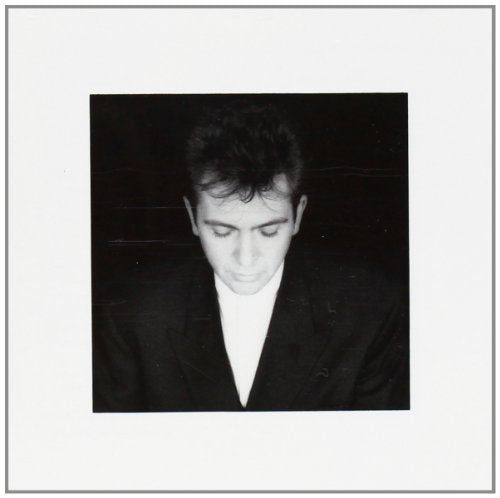 Black and white portrait of Peter Gabriel looking downwards, wearing a suit.