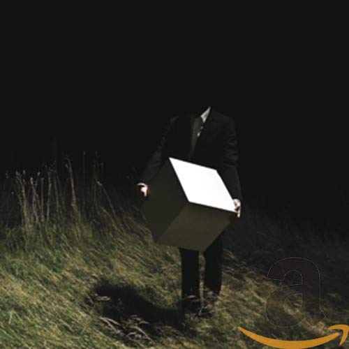 Person in suit holding a white cube over their head in a field.