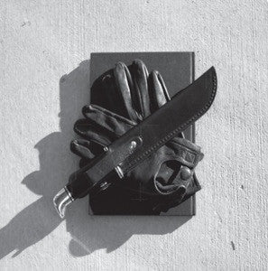 Black and white image of gloves and a knife on a surface.